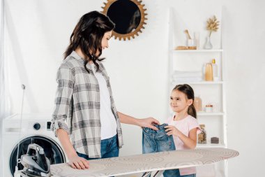 Anne ve kızı ayakta Ütü Masası yakınındaki ve kot pantolon çamaşır odasında holding