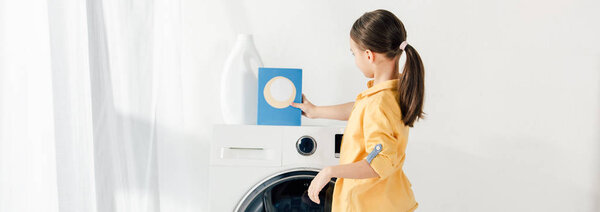 panoramic shot of child standing near washer and putting washing powder in laundry room