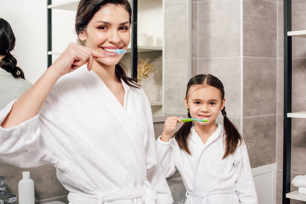 mother and daughter brushing teeth with toothbrushes in bathroom