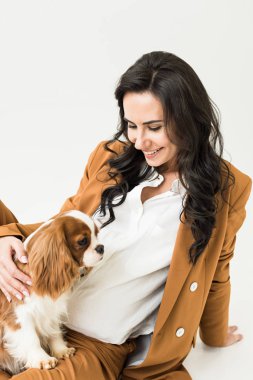 Beyaz arka plan üzerinde kahverengi ceket okşayarak köpek hamile kadın gülüyor