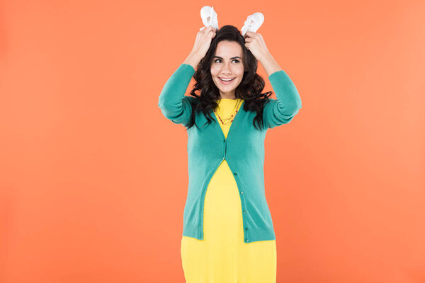 Funny pregnant woman holding baby shoes isolated on orange