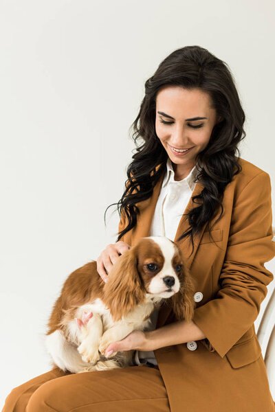 Attractive curly woman in brown jacket holding dog isolated on white 