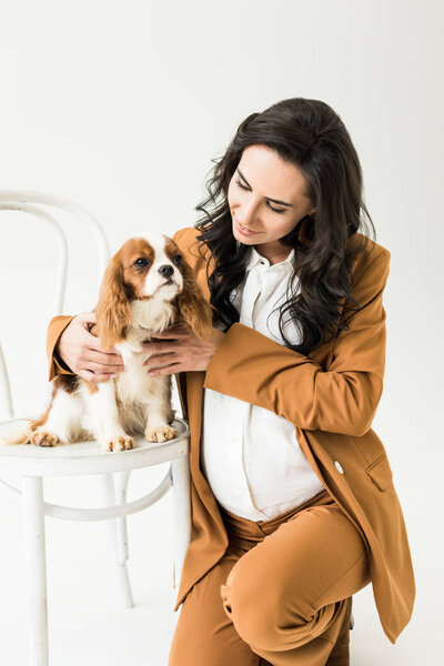Cheerful pregnant woman sitting near dog on chair isolated on white 