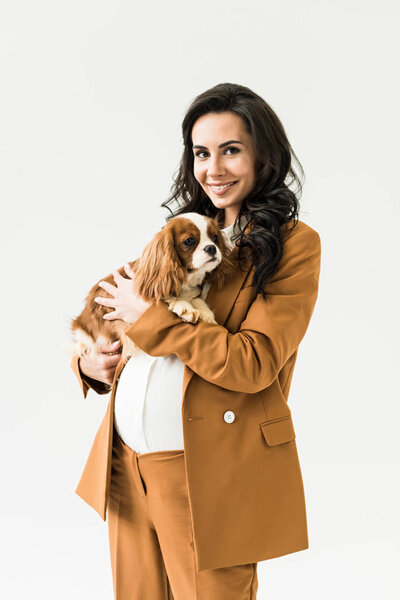 Charming pregnant woman in suit holding dog isolated on white