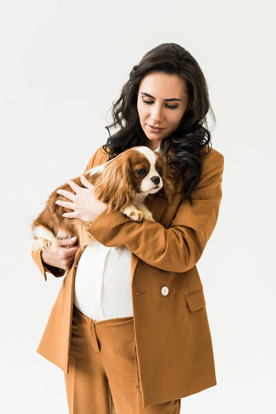 Curly pregnant woman in brown suit holding dog isolated on white