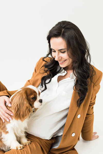 Laughing pregnant woman in brown jacket stroking dog on white background