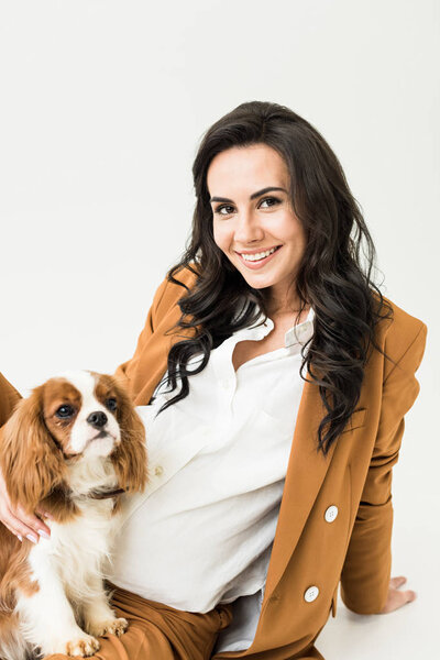 Attractive pregnant woman in brown jacket stroking dog on white background