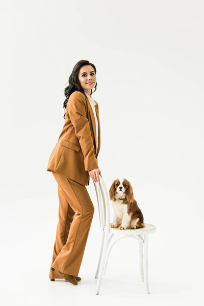 Amazing pregnant woman in suit standing near dog on chair on white background