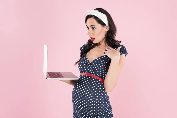 Verbaasd Zwangere Vrouw Gestippelde Jurk Kijken Laptop Scherm Geïsoleerd Roze — Stockfoto