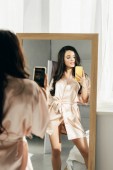 attraktive brünette Frau fotografiert, während sie in der Nähe von Spiegel steht