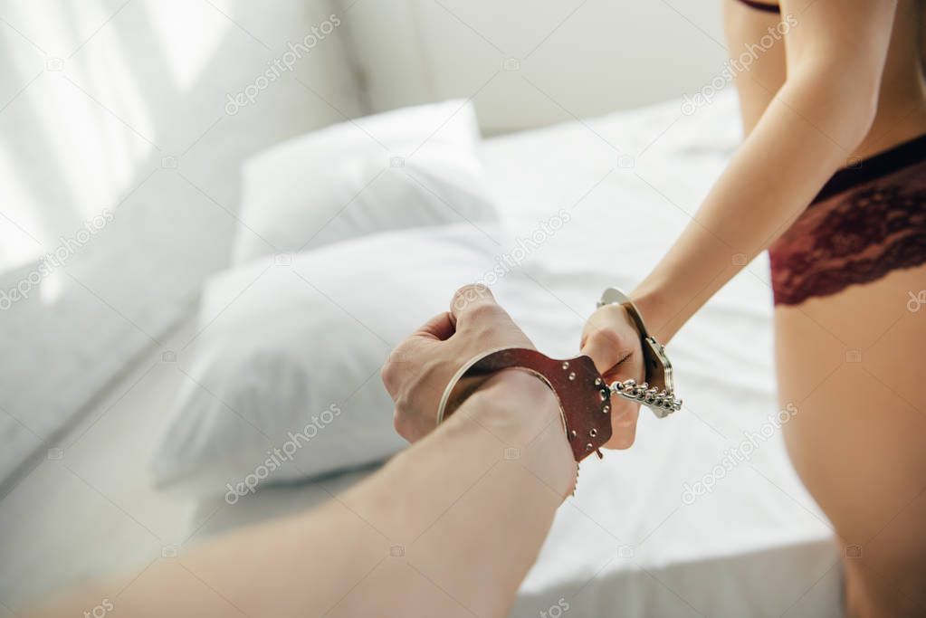 cropped view of man handcuffed with woman in white modern bedroom 