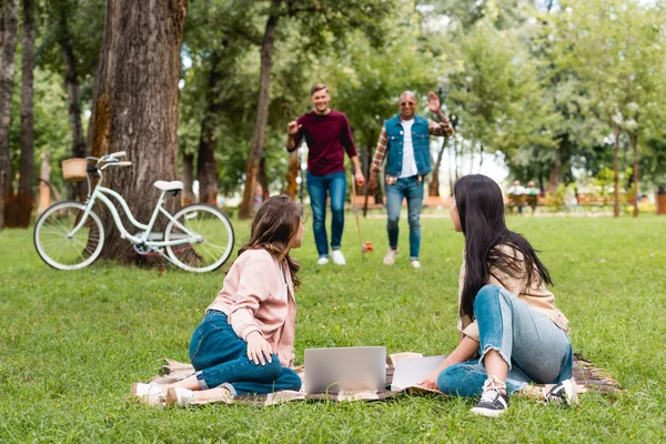 seçici odak battaniye laptop ve neşeli çok kültürlü insanlar ellerini sallayarak peşinde yakın oturan genç kadınların