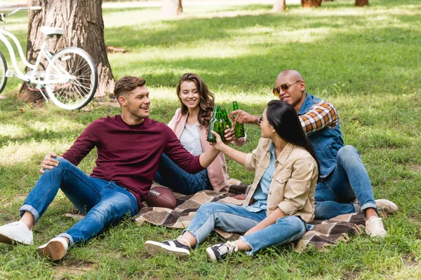 格子縞の毛布の上に座って 公園でボトルをチリンと友人の民族グループ — ストック写真