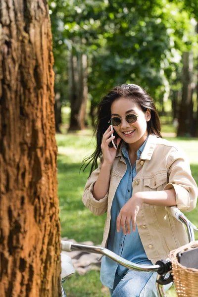 Lächelnde Junge Frau Mit Sonnenbrille Spricht Auf Smartphone Neben Fahrrad — Stockfoto