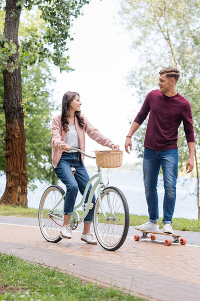 handsome man longboarding and looking at attractive girlfriend riding bicycle 