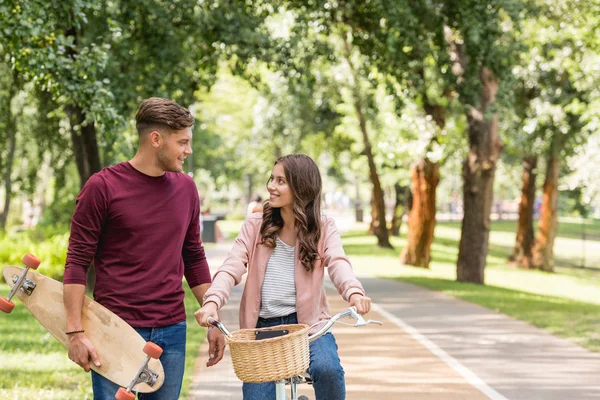 Όμορφος Άνδρας Κρατώντας Longboard Και Βλέπουν Ελκυστική Φίλη Ιππασία Ποδήλατο — Φωτογραφία Αρχείου