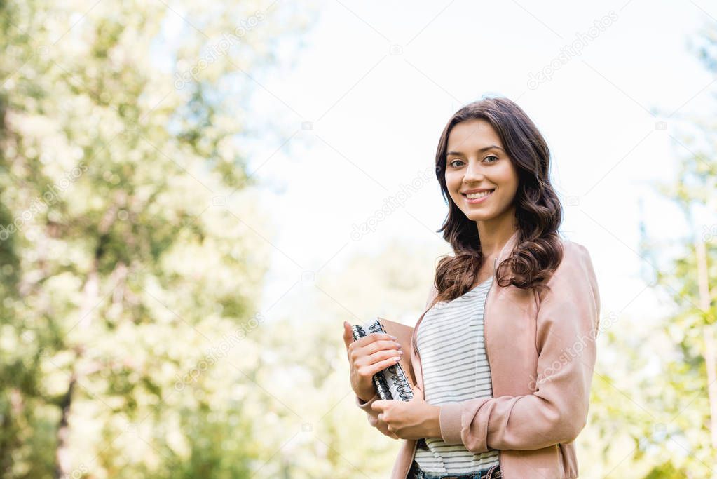 beautiful young woman holding books and smiling in park