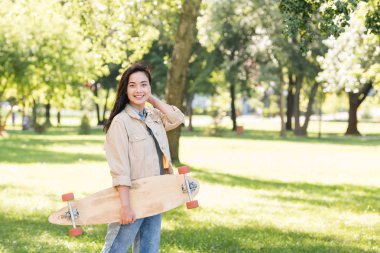 neşeli güzel kız parkta longboard tutarken gülümseyen 