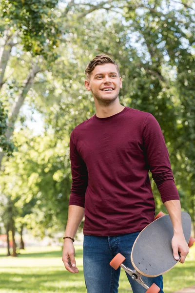 Bonito Jovem Homem Sorrindo Enquanto Segurando Longboard Parque — Fotografia de Stock