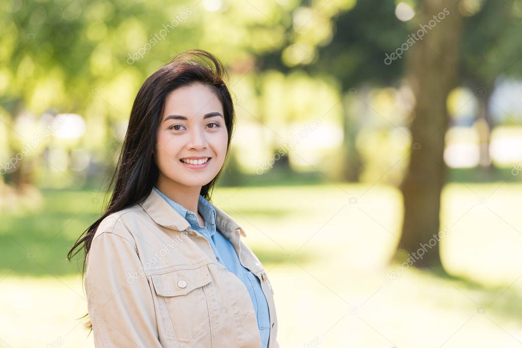 cheerful young woman smiling while looking at camera in park
