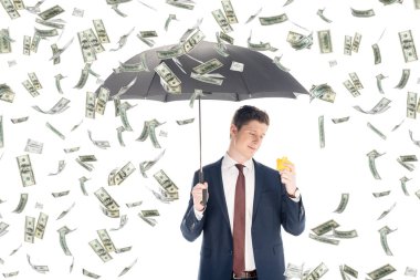 successful businessman in suit holding umbrella and yellow piggy bank under money rain on white background clipart