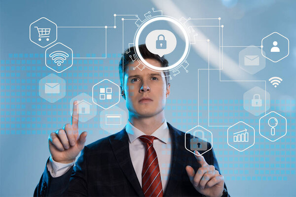 handsome businessman in suit pointing with fingers at cyber security icons in front on blue background