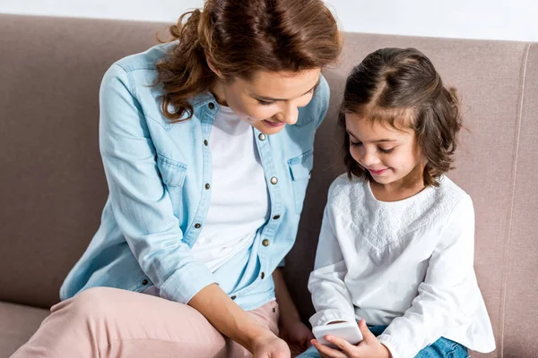 Hymyilevä Äiti Tytär Istuvat Sohvalla Käyttävät Älypuhelinta — kuvapankkivalokuva
