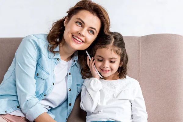 Blissful Mother Daughter Sitting Brown Sofa Talking Smartphone Isolated White — Stock Photo, Image