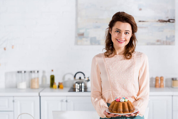 Smiling happy woman holding plate with easter bread in kitchen