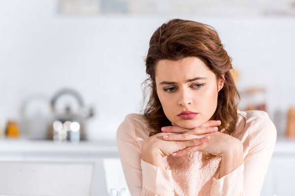 Расстроенная темноволосая привлекательная женщина с переплетенными пальцами, смотрящая вниз
