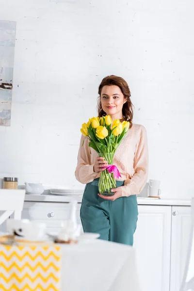 Blissful Curly Woman Holding Bouquet Yellow Tulips Kitchen — Stock Photo, Image