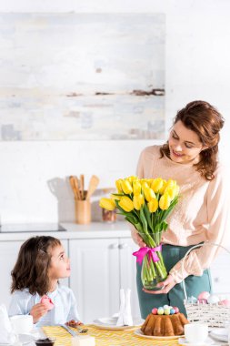 Acıbadem kurabiyesi yeme ve Lale buketi mutfakta annesine bakarak çocuk