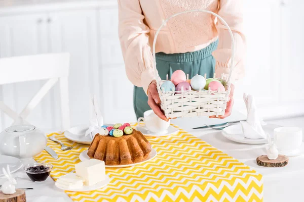 Cropped View Woman Holding Wicker Basket Painted Easter Eggs Table — Stock Photo, Image