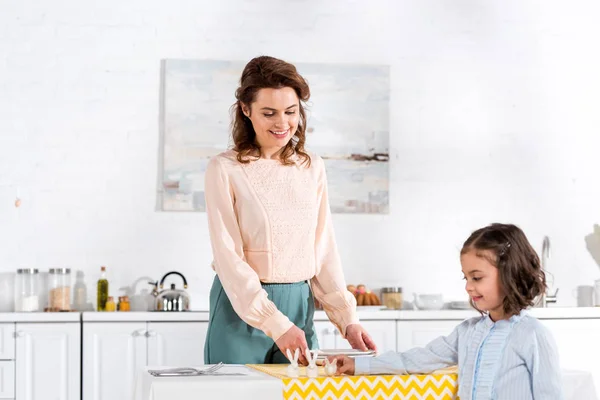 Sorrindo Mãe Olhando Para Filha Enquanto Servia Mesa Cozinha — Fotografia de Stock