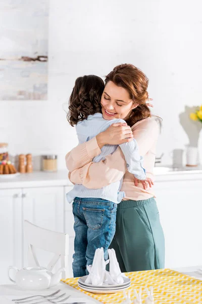 Sorrindo Mãe Abraçando Criança Encaracolado Cozinha Perto Mesa — Fotografia de Stock