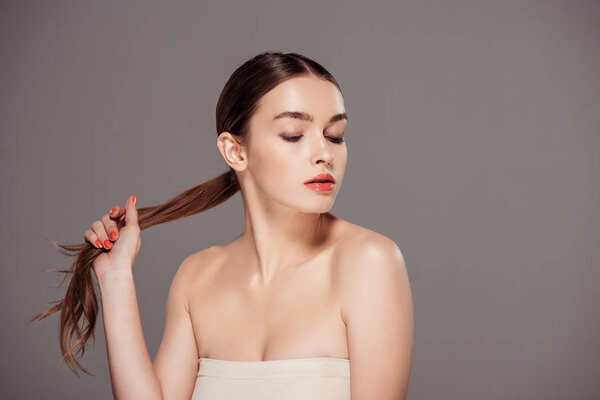 красивая стильная девушка касаясь волос и позируя изолированы на сером с копировальным пространством
