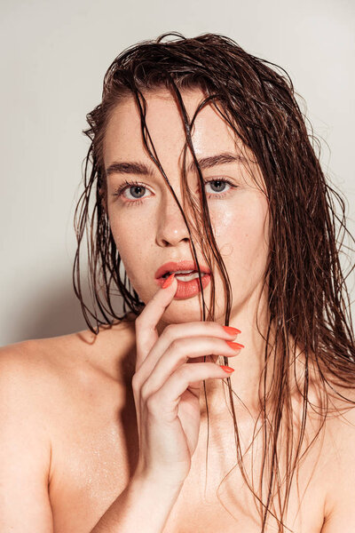 beautiful young woman with coral lips and wet hair gesturing and looking at camera on grey background
