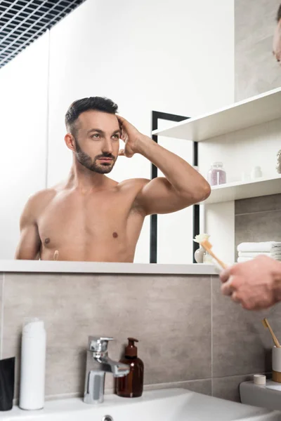 髪に触れると 浴室の鏡を見ながら歯ブラシを保持しているハンサムな上半身裸の男 — ストック写真