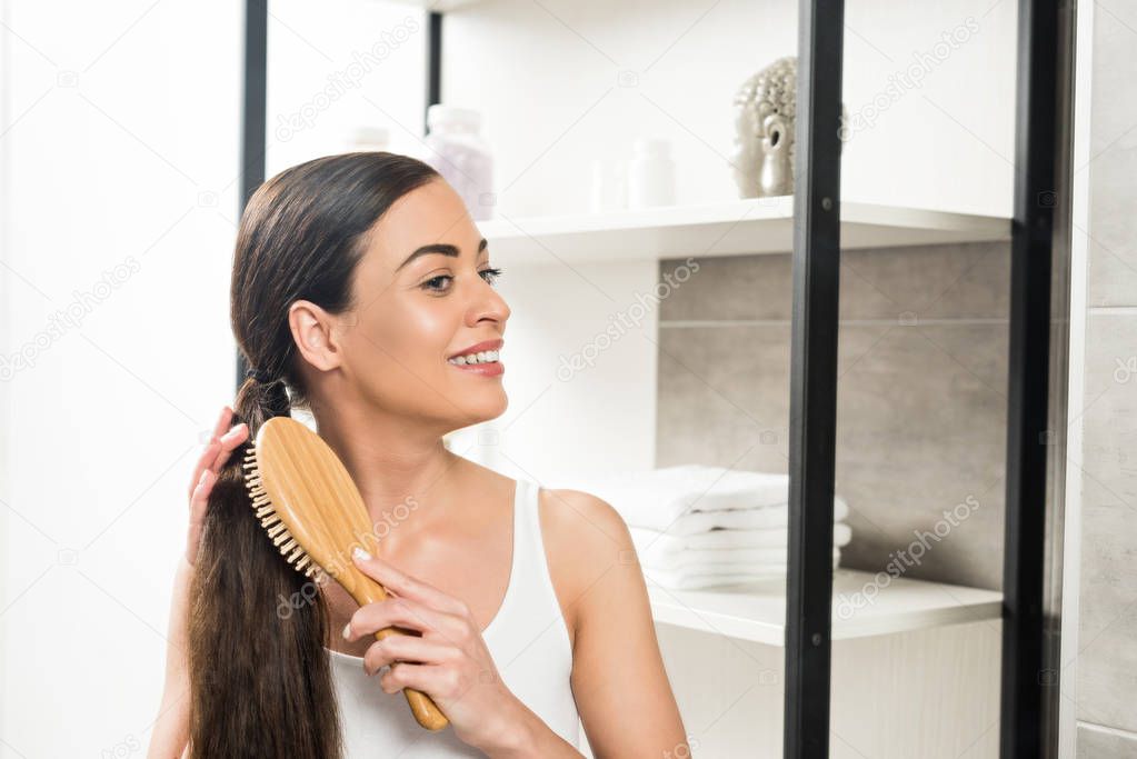 cheerful brunette woman brushing hair in bathroom 
