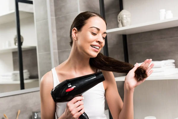 Mujer Morena Feliz Sosteniendo Secador Pelo Mientras Está Pie Baño — Foto de Stock