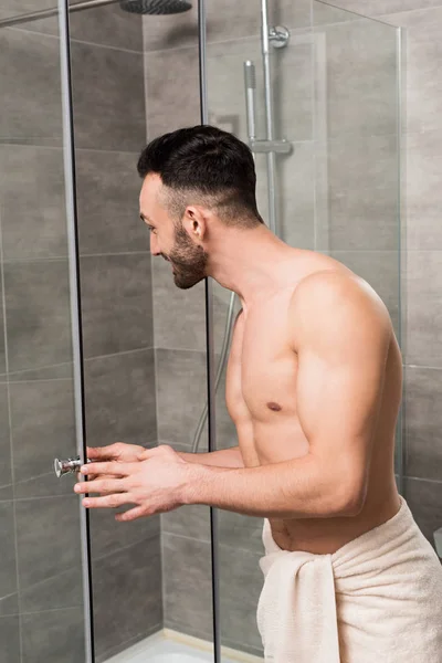 muscular shirtless man standing near shower cabin in bathroom