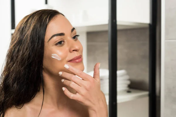 Bella Donna Che Applica Crema Viso Sulla Guancia Mentre Guarda — Foto Stock