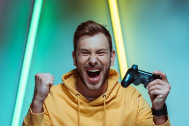  handsome and screaming man looking at camera and holding gamepad clipart