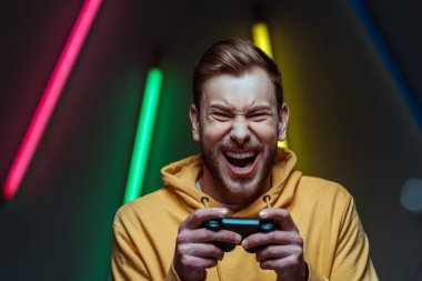 handsome and screaming man looking at camera and holding gamepad clipart