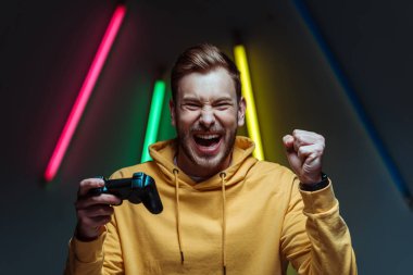 young adult handsome and screaming man looking at camera and holding gamepad clipart