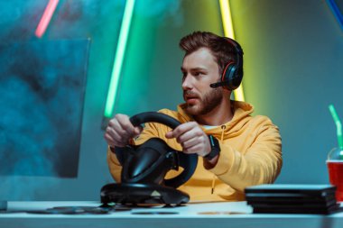 young adult and handsome man in headphones playing video game with steering wheel clipart