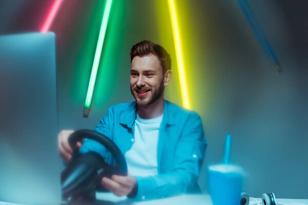 избирательный фокус красивого и улыбающегося мужчины, играющего в видеоигру с рулем
