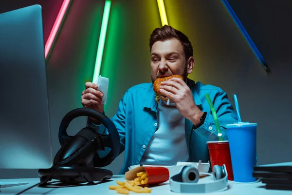 Όμορφος Και Ωραίος Άνθρωπος Τρώγοντας Burger Και Κοιτάζοντας Την Οθόνη — Φωτογραφία Αρχείου