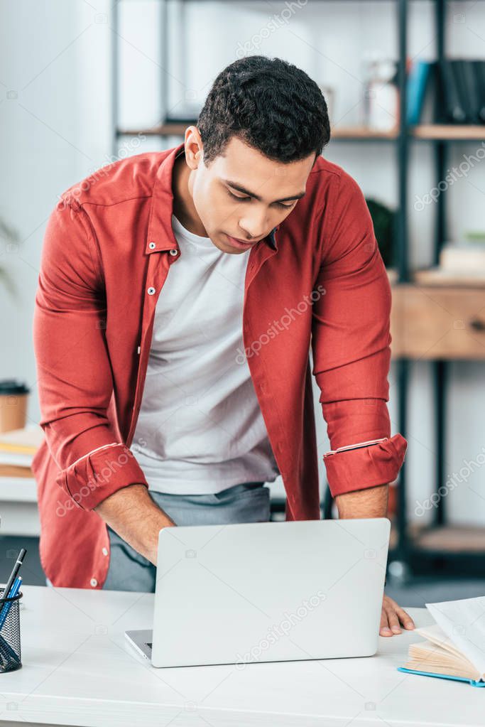 Concentrated student in red shirt using laptop at workplace