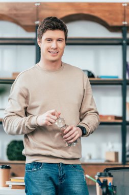 Jeans açılan su şişesi ve kamera görünümlü gülümseyen genç adam